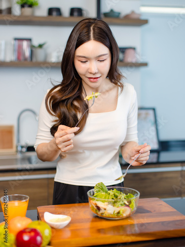 Asian young pretty positive woman standing in kitchen prepare making eating healthy salad from glass bowl cooking healthy food fresh vegetables fruits clean feel good morning happy relaxing lifestyle.