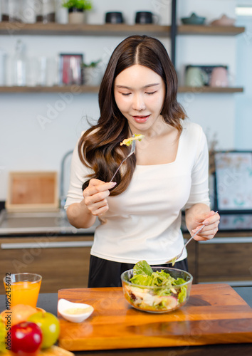 Asian young pretty positive woman standing in kitchen prepare making eating healthy salad from glass bowl cooking healthy food fresh vegetables fruits clean feel good morning happy relaxing lifestyle.