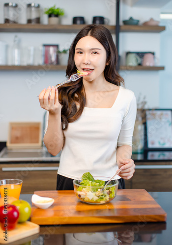 Asian young pretty positive woman standing in kitchen prepare making eating healthy salad from glass bowl cooking healthy food fresh vegetables fruits clean feel good morning happy relaxing lifestyle.