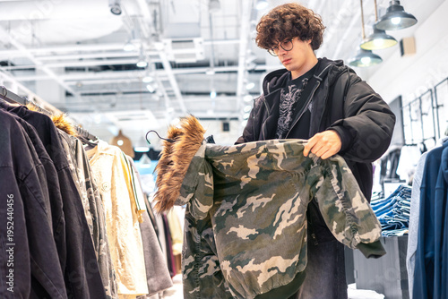 Foto Teenage Boy Choosing Camouflage Jacket in Clothing Store, Youth Fashion Shopping
