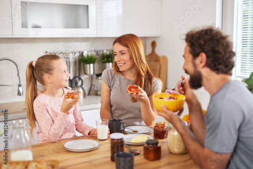 A family shares a joyful breakfast moment in their bright kitchen, engaging in conversation while enjoying toast and cereals together.