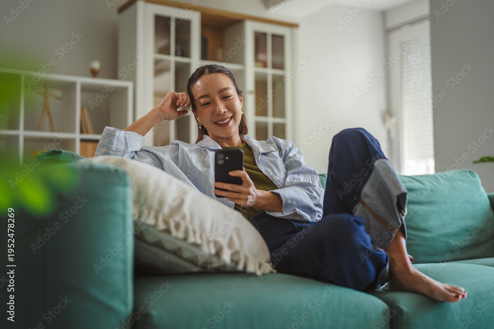 Fototapeta premium Asian woman relaxing on couch using smart phone