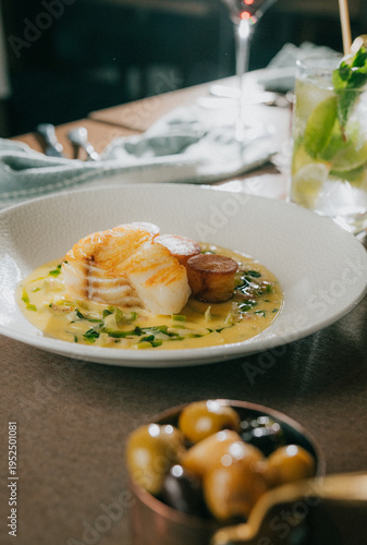 Canvastavla Seared scallop rests in golden sauce beside a small garnish
