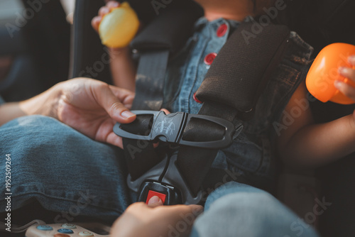 Close up of a mother's hands securely fastening a safety harness on a toddler in a car seat. Concept of child protection, parental care, and road safety during a family trip. Highlighting the importan
