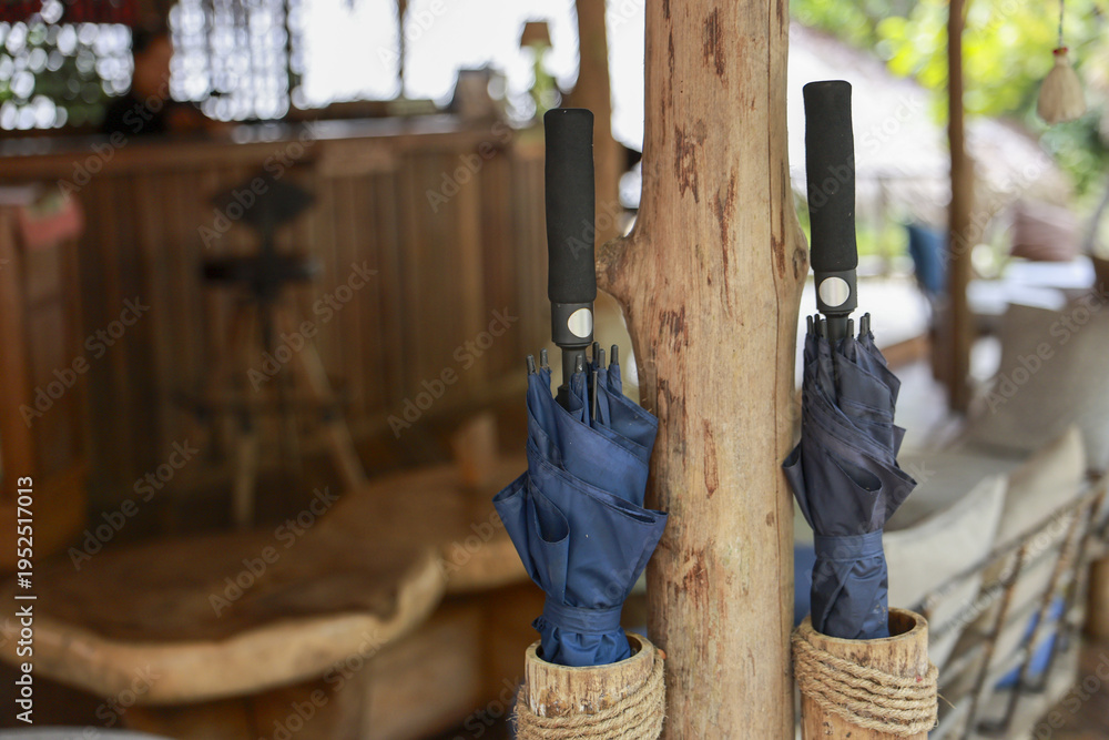 Fototapeta premium Two blue umbrellas waiting in rustic woven holder inside wooden resort lobby. calm and prepared atmosphere, ready for rainy day or tropical weather