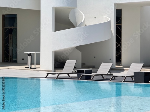 Outdoor swimming pool area with luxury sun loungers and modern white spiral staircase.