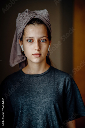 Natural portrait of a teen girl after a shower, with a towel on her head and earphones. Home lifestyle image for themes of morning routine, self care, natural skin and teenage everyday life.