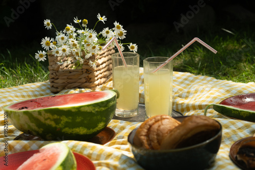 Summer picnic food. Two glasses of lemonade, watermelon, pastries on yellow and white blanket. Summertime vibes. 