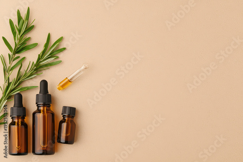 Flat lay of amber essential oil bottles with droppers and fresh green rosemary sprigs on beige background, evoking natural wellness and calmness