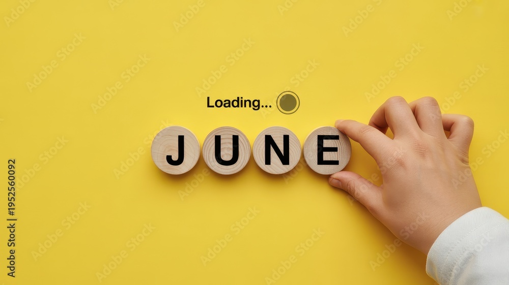 Fototapeta premium Hand placing a wooden block with the letter 'E' to complete the word 'JUNE' on a yellow background, with loading text.