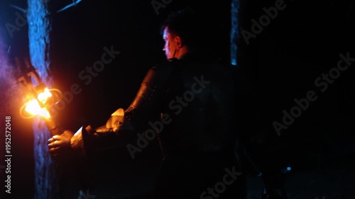 A knight in full armor, holding a sword and torch, walks through a dark night forest, seen from behind. A medieval warrior in the dark. Video with sound.
