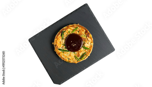 Round savory pancake with brown sauce on a rectangular black slate against a black background