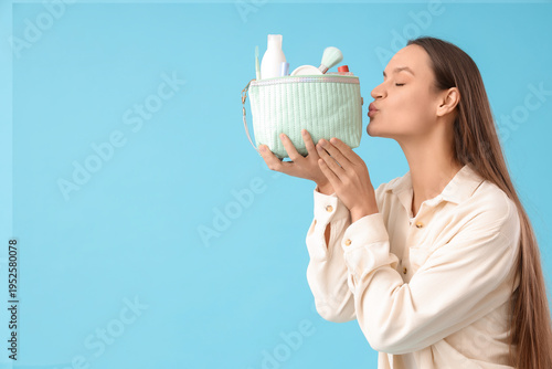 Bild auf Leinwand Young woman kissing cosmetic bag full of makeup products on blue background