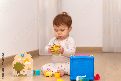 9-month-old infant girl sitting on the floor and playing with toys.