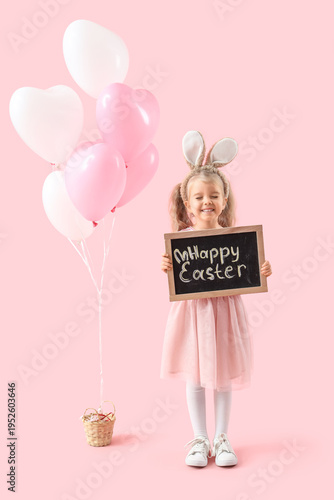 Cute little girl in bunny ears holding chalkboard with text HAPPY EASTER on pink background