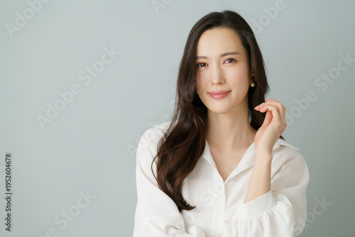 Obraz na płótnie グレーバックの頬に手を当てる白いシャツを着た若い日本人女性のポートレート