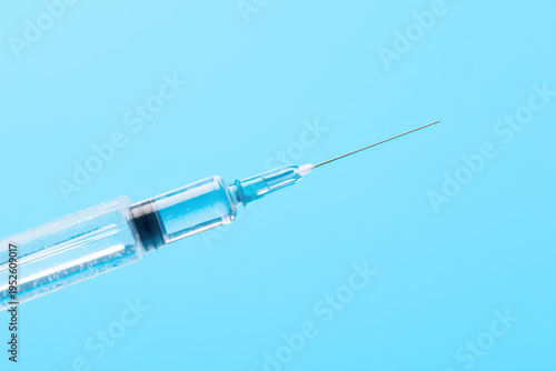Syringe needle close up with transparent liquid inside on blue background, medical injection tool for healthcare and vaccination use, clean and sterile equipment