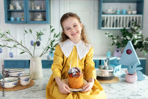 Wallpaper Mural Young girl sit on kitchen with cake, spring decor, flowers, easter eggs and bunny. Child Girl in yellow dress holding easter cake on plate in hands. Little Girl preparing festive pastries at home. Torontodigital.ca