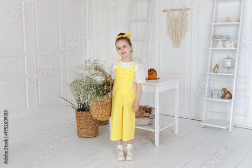 Wallpaper Mural Young girl is standing and holding basket with gypsophila flowers. Pretty little girl in yellow overalls with rustic bouquet of flowers in wicker bag on light background. Mother day. Torontodigital.ca