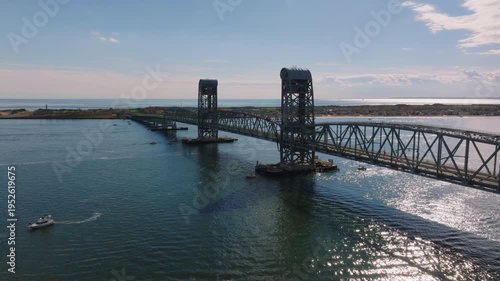 Aerial drone view of Marine Parkway Bridge spanning calm coastal water with surrounding shoreline and breakwater under a soft cloudy sky.