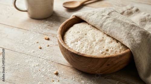 Rustic wooden bowl holding an active sourdough bread dough covered with a linen cloth, showing bubbles from fermentation on a flour dusted kitchen table
