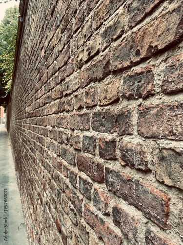 Fotografía Strong low-angle perspective shot along the length of a centuries-old red brick wall with deeply textured and weathered surface