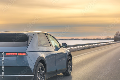 Electric vehicle driving on winter highway at sunset through snowy landscape. EV road travel.