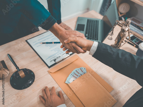 The lawyer shakes hands with his client after signing a settlement or compromise agreement. A gavel, scales, and legal documents are on the wooden table.