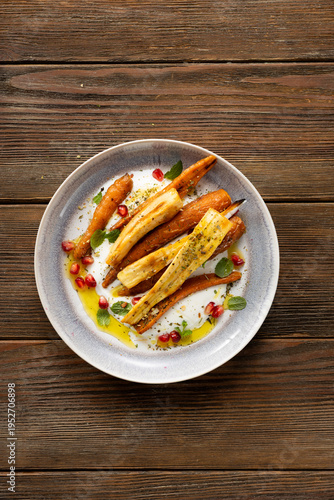 Top view of whole roasted carrots and parsnip slices on cheese on plate