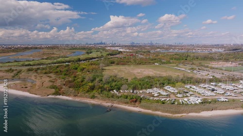 Aerial drone view of a coastal landscape with shoreline, open land, and scattered structures under a bright sky, showing natural terrain and waterfront area.