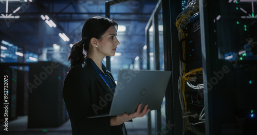 Technician uses a laptop computer to check and monitor server racks in a large data center, hardware installation, network devices diagnosttics, system check. Server room with mainframes.
