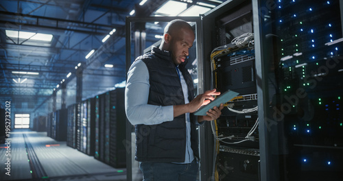 Data center technician inspects server racks, checks network cables, and uses a tablet to monitor hardware status. Rows of illuminated servers, digital infrastructure, and secure network operations.