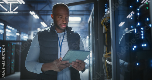 Obraz na płótnie Data center technician inspects server racks, checks network cables, and uses a tablet to monitor hardware status