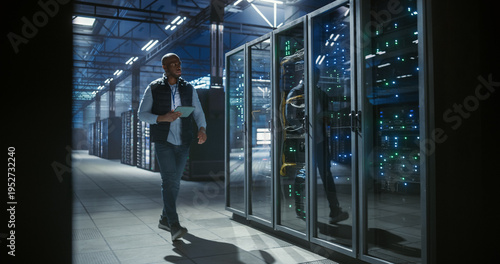 Quadro em tela Data center IT specialist walks through aisles of server racks, using a tablet t