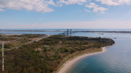 Aerial drone view of Marine Parkway Bridge spanning calm coastal water with surrounding shoreline and breakwater under a soft cloudy sky.