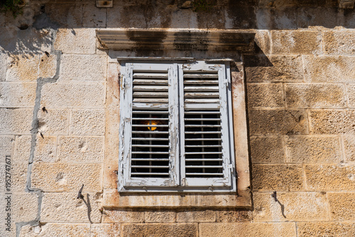 Weathered white wooden shutters on an old stone wall, rustic Mediterranean architectural detail in bright sunlight.