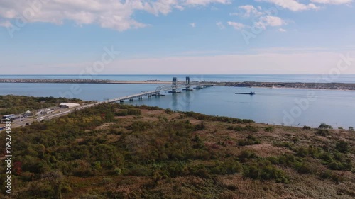 Aerial drone view of Marine Parkway Bridge spanning calm coastal water with surrounding shoreline and breakwater under a soft cloudy sky.