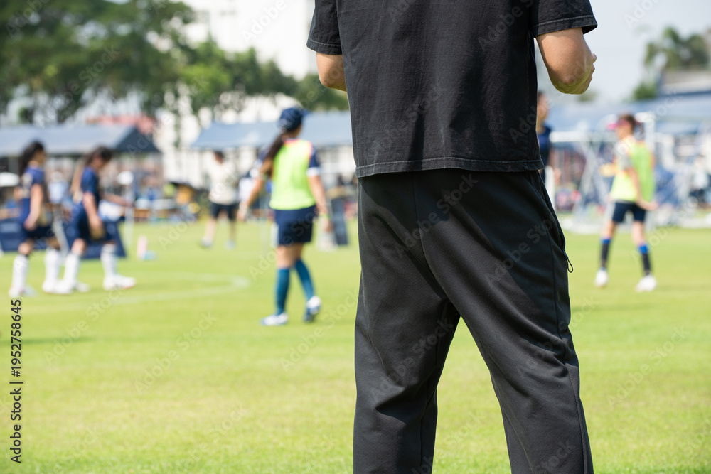 Fototapeta premium Asian parents watching and supporting their children playing football on a sunny afternoon at a local community tournament.