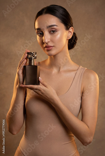 A beautiful sexy lady in an elegant nude bodysuit holds a bottle in her hands. Fashion beauty portrait of fashion model