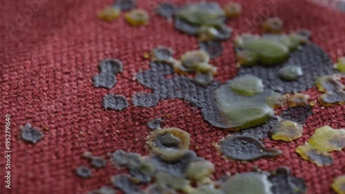 Dripping yellow and green candle wax stains onto cloth or furniture upholstery on a burgundy background. Concept of everyday life problem and home cleaning