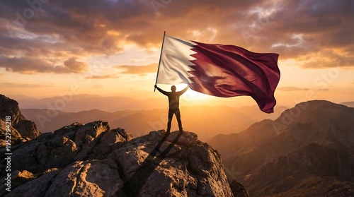 Silhouette of a person holding the flag of Qatar aloft on a rocky mountain peak at sunset with dramatic clouds and golden light