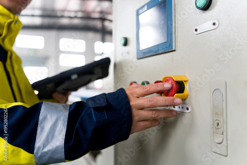 Worker operating industrial control panel and pressing emergency stop button
