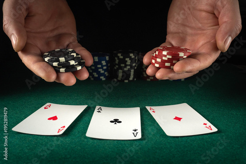 Two hands are seen holding stacks of red, black, and white poker chips. Three playing cards lay face up on the green table. The scene shows the action of a card game in low light