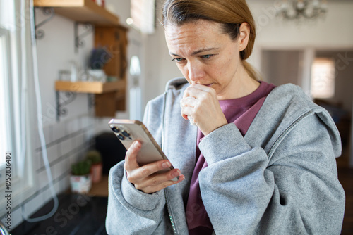 Cuadro en lienzo Concerned woman reading message on smartphone in home kitchen