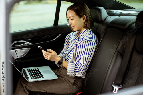 Korean woman uses laptop and phone while sitting in a car during a busy day