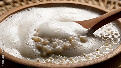Close-up of a wooden spoon stirring a frothy white liquid in a rustic bowl.