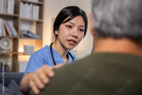 Empathetic female Asian nurse in blue scrubs consulting senior patient at home clinic room showing genuine care support comfort and understanding during difficult medical discussion