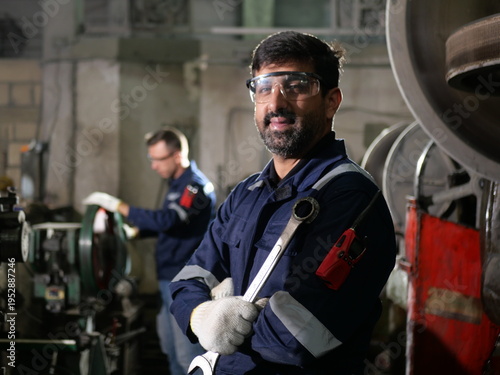 Confident industrial worker holding wrench in factory workshop