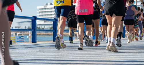 Marathon participants running beside blue railings on waterfront promenade
