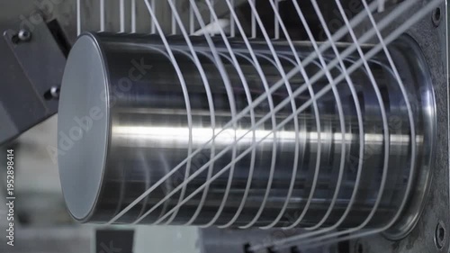 High-speed rotation of white threads on a metal cylinder during the textile weaving process in a factory.